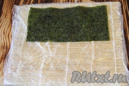 Подготовить циновку, я предварительно оборачиваю циновку пищевой плёнкой и смазываю её тонким слоем майонеза. Выложить лист нори блестящей стороной вниз.