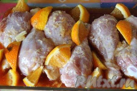 В форму для запекания выкладываем куриные ножки вместе с апельсиновым соком, в котором они мариновались, затем раскладываем чеснок и апельсин. Накрываем форму для запекания крышкой (или фольгой) и отправляем в разогретую духовку, запекаем 35 минут при температуре 180 градусов. Затем снимаем крышку (или фольгу) и готовим ещё 15 минут.