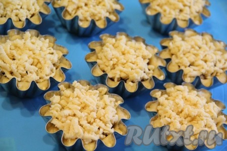 Достать оставшееся тесто из морозильной камеры и натереть его на крупной тёрке. Выложить кусочки теста поверх варенья, как бы создавая "шапочку". Переставить корзинки на противень для выпекания и поставить в разогретую духовку. Выпекать корзиночки с вареньем при 180-200 градусах примерно 20-25 минут до золотистого цвета.