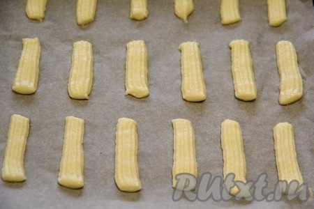 Противень для выпечки застелить пергаментной бумагой. Переложить тесто в целлофановый пакет, отрезав уголок, или в кондитерский мешок и отсадить белое тесто в виде полосок длиной примерно 5 сантиметров.
