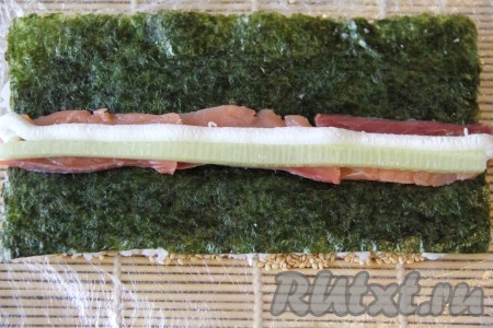 Одной половинкой циновки покрыть верх риса с кунжутом и слегка прижать, а затем аккуратно перевернуть. Таким образом у нас получится наверху лист нори. Выложить начинку по середине, последовательность не имеет значения. Я выложила рыбу, огурец и брынзу.