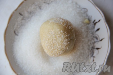 Отщипываем от теста небольшие кусочки и скатываем их в шарики размером с грецкий орех. 50 грамм сахара насыпаем в тарелку. Полученные шарики обваливаем со всех сторон в сахаре.