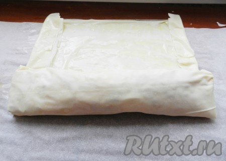 Подвернуть боковые края теста немного на начинку, а затем свернуть в рулет, начиная со стороны с яблочной начинкой.