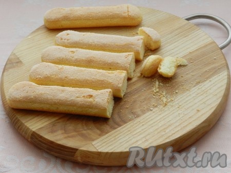 Дно разъёмной формы для выпечки диаметром 18-20 сантиметров застелить бумагой для выпечки, чтобы бумага свисала по краям. Смазывать форму не нужно. Печенье "Савоярди" обрезать с одного края примерно на 1 сантиметр для устойчивости.