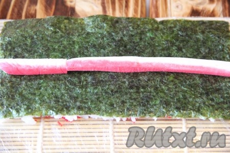 Одной половинкой циновки покрыть верх риса с икрой и слегка прижать, а затем аккуратно перевернуть. Таким образом у нас получится наверху лист нори. Выложить полоски крабовых палочек.