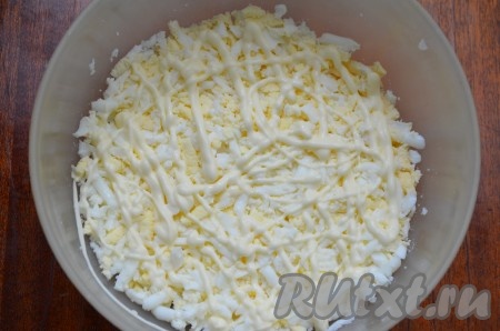 Яйца отварить в течение 10 минут с момента закипания воды, остудить их и очистить. Варёные яйца натереть на крупной тёрке, выложить на дно салатника. Сделать сеточку из майонеза.