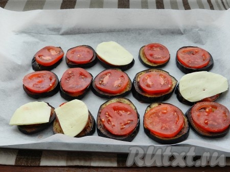 Небольшой противень застелить бумагой для выпечки. Выложить обжаренные баклажаны. На каждый кружочек баклажана положить кружочек помидора.