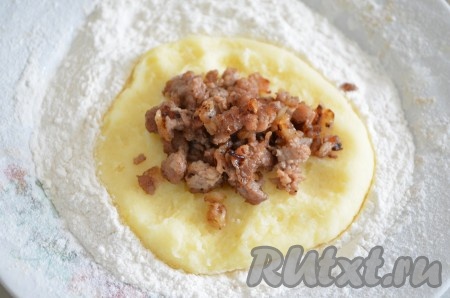 Из картофельной массы сформировать небольшую лепёшку, выложить на поверхность, припылённую мукой. В центр лепёшки выложить 2 чайные ложки начинки, аккуратно защипнуть края лепёшки так, чтобы фарш оказался внутри.
