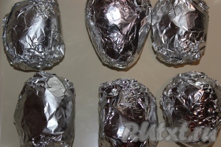 Отправить картофель в мундире, завёрнутый в фольгу, в духовку, разогретую до 200 градусов, и запекать около часа (до готовности). Для проверки готовности можно проткнуть картофелину деревянной зубочисткой (если входит легко - картошечка готова).