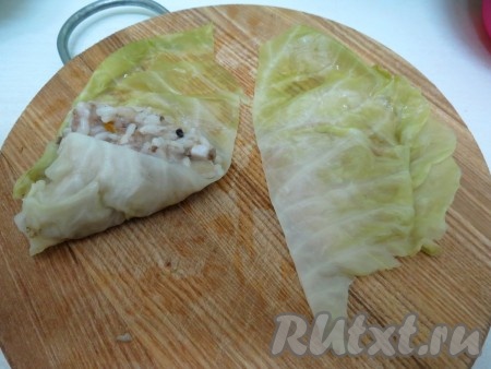 На каждую половинку выкладываем приблизительно 1 десертную ложку фарша по центру, подворачиваем вверх один угол капусты, а затем второй. У нас получаются маленькие треугольники.
