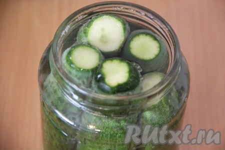 Как только маринад закипит, влить в кастрюлю уксус, перемешать и залить горячим маринадом баночки с огурцами.
