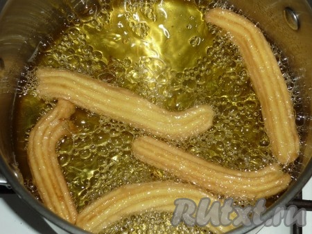 В сотейник налить растительное масло и сильно разогреть его. В раскаленное масло небольшими партиями выдавливать заварное тесто, отрезая тесто ножницами. Жарить чуррос до золотистого цвета, затем выкладывать на бумажное полотенце, чтобы избавиться от лишнего жира.
