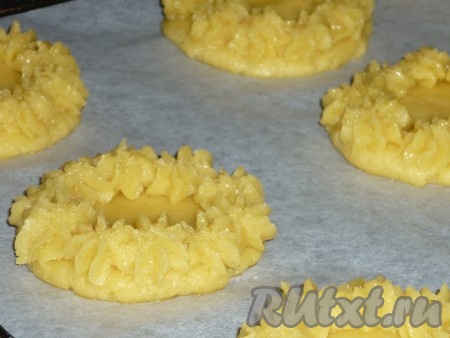 По истечении времени достать тесто из холодильника и разделить на 2 части. Одну часть теста на слегка присыпанной мукой поверхности раскатать в пласт (тонко раскатывать не нужно). Из теста с помощью стакана вырезать кружочки. Переложить кружочки на противень, застеленный пергаментной бумагой. Вторую часть песочного теста поместить в кондитерский мешок и с помощью насадки сделать бортики на каждом кружке, формируя неглубокие корзиночки.