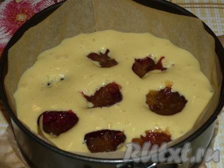 В форму для выпечки, застеленную пергаментом, вылить половину теста. Сливы вымыть, разделить пополам и, удалив косточку, выложить в форму на тесто.&nbsp;
