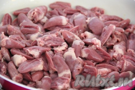 Куриные сердечки откинуть на дуршлаг, чтобы стекла лишняя жидкость, затем разрезать на две части. В сковороду влить масло и выложить сердечки.
