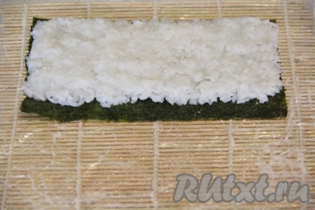 Подготовить циновку.&nbsp;Лист нори разрезать на две части. На циновку положить лист нори блестящей стороной вниз. Выложить часть риса и разровнять его по поверхности листа нори, оставив пустым дальний от вас край шириной 1 см. Чтобы рис не прилипал к рукам, можно руки смочить в подкисленной воде (я в мисочку с водой капаю пару капель лимонного сока или добавляю кристаллы лимонной кислоты).