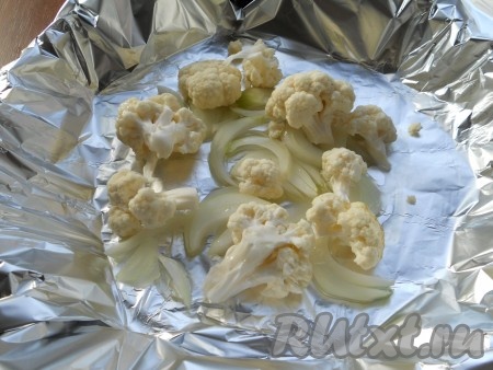 Форму для запекания застелить фольгой в 2 слоя. Влить растительное масло. Лук нарезать крупными полукольцами, капусту цветную разобрать на соцветия. Поместить лук и капусту в форму. Чуть посолить.
