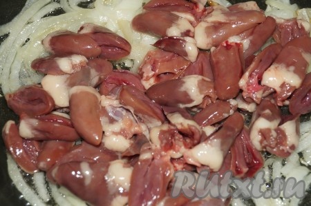 Обжарить лук, помешивая, на растительном масле до легкого золотистого цвета. Куриные сердечки, вымыть, срезать все прожилки, разрезать пополам, добавить к обжаренному репчатому луку и жарить до готовности минут 10-15 (крышкой накрывать не надо), периодически помешивать.
