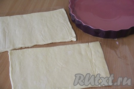 Размороженное слоеное тесто слегка раскатать и, в зависимости от размера формы для выпечки, разрезать на две неравные части (большая часть раскатанного теста станет основой пирога, а меньшую часть теста можно использовать для украшения). Я немного теста оставила для украшения верха пирога.
