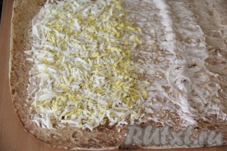 Яйца очистить от скорлупы и натереть на крупной тёрке. Выложить измельчённые яйца на лаваш ровной и плотной полоской.
