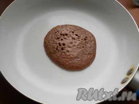 Панкейки жарятся на сухой сковороде, но если поверхность сковороды не очень качественная, тогда немного смажьте её растительным маслом. В центр хорошо разогревшейся сковороды влить 2-3 столовых ложки шоколадного теста. Жарить панкейк на небольшом огне с одной стороны до тех пор, пока сверху не появятся крупные дырочки (примерно 1-1,5 минуты).