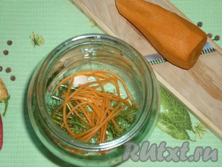 Выложить на дно каждой простерилизованной банки 1-2 зонтика укропа, 3-4 горошинки чёрного перца и 2 очищенных зубчика чеснока. Очистить морковь, натереть на тёрке для корейской морковки. Выложить немного моркови на дно каждой баночки.

