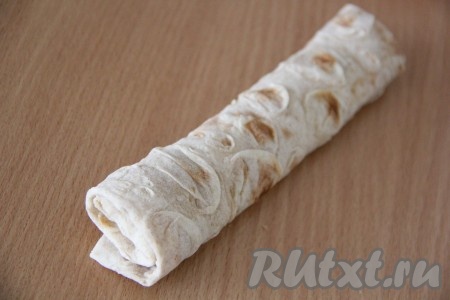  Подвернуть боковые края лаваша на начинку, а затем свернуть лаваш в плотный рулетик, начиная со стороны с начинкой.