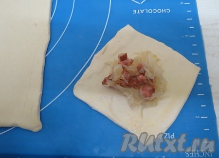 На каждый квадрат выкладываем начинку из квашеной капусты и колбасы. В мисочку разбиваем яйцо и вилкой соединяем желток с белком. Яйцом смазываем края пирожка, стараясь, чтобы яйцо не попало на линию среза (если яйцо попадёт на линию среза, пирожки будут плохо "расти" в духовке).
