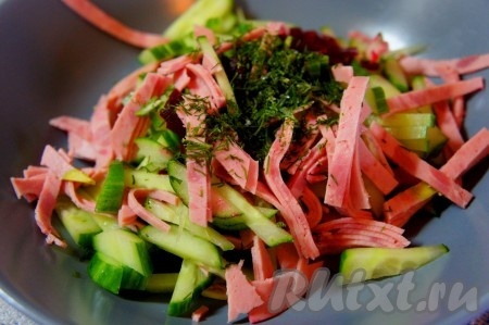 В тарелку положить нарезанные огурец и колбасу, добавить зелень.