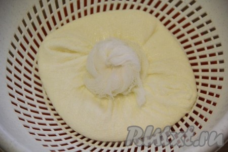 На некоторое время оставить марлю с творогом на дуршлаге, чтобы стекла лишняя сыворотка, а затем завязать марлю узлом, а сверху поставить груз.
