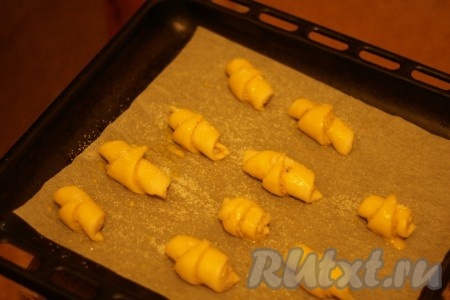 Выложить рогалики на противень, застеленный бумагой для выпекания, смазать их желтком и посыпать сахаром.
