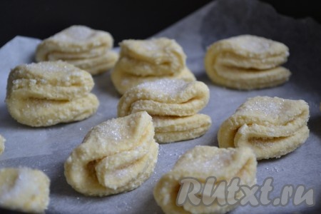 Каждый вырезанный кружочек сложить 2 раза пополам, потом присыпать сверху сахаром и переложить на противень, застеленный бумагой для выпечки. У нас получатся заготовки печенья "Ушки", как на фото. Выпекать печенье в разогретой духовке при температуре 150 градусов 15 минут. Затем духовку выключить и оставить выпечку в ней ещё на 2-4 минуты.