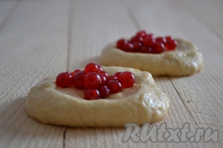 Пока тесто подходит, нужно вымыть смородину, отделить от веточек, обсушить, выложив на полотенце. Если планируете готовить с замороженной смородиной, тогда разморозьте её, лишнюю жидкость слейте. Поднявшееся тесто обмять, разделить на равные кусочки. Каждый кусочек растянуть в лепёшку и выложить в центр подготовленную начинку (ягоды смородины).