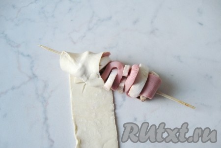 Обвернуть полоску слоёного теста внахлёст вокруг сосиски с грибами. Если одна полоска закончится, кладите следующую, слепив края теста.