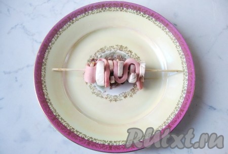 Полоску сосиски и нарезанные пластины грибов одеть на деревянную шпажку, чередуя шампиньоны и сосиску.