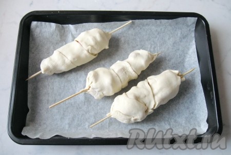 Выложить сформированную сосиску в тесте в форму для запекания, застеленную пергаментной бумагой. Аналогично сформировать все сосиски на шпажках в тесте.