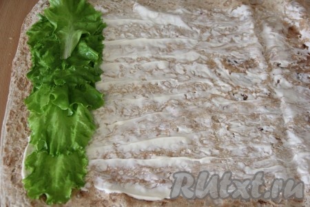 Лист лаваша смазать майонезом. Для лучшего и аккуратного формирования рулета, края лаваша лучше оставить чистыми. Затем выложить листья салата и сформировать плотную полоску.
