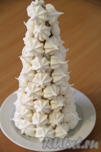 Обмакнуть плоскую часть безе в растопленный шоколад и прикрепить к каркасу ёлки. Слегка придавить и подождать, когда шоколад схватится. Таким образом прикрепить всё безе к каркасу ёлки. Поставить ёлочку в холодильник на 30 минут, чтобы шоколад полностью застыл. Наша ёлка готова, осталось только декорировать её.