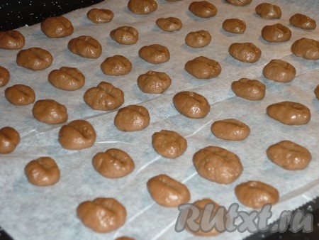 Отщипывая от теста небольшие кусочки, скатывать их в шарики и выкладывать на противень, застеленный пергаментом, на расстоянии друг от друга. Затем к поверхности шариков приложить зубочистку, придавая заготовкам печенья форму кофейных зёрен. Отправить противень в разогретую до 180 градусов духовку, выпекать печенье 10-15 минут.&nbsp;