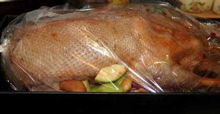 На дно рукава для запекания кладём несколько кусочков яблок с айвой. В рукав для запекания выкладываем фаршированную утку, завязываем рукав с двух сторон.