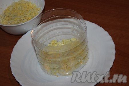 Яйца отварить вкрутую, охладить, очистить, натереть на средней терке. На плоскую тарелку поставить бортики для формирования салата. Я сделала бортики, разрезав пластиковую бутылку. Часть яиц, натертых на терке, выложить первым слоем, немного посолить, слегка смазать майонезом.
