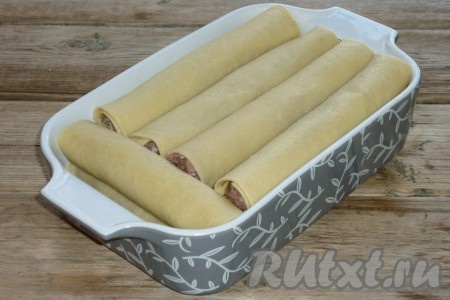 Свернуть тесто в трубочку, начиная со стороны с фаршем, и выложить в жаропрочную форму. Аналогично сформировать все домашние фаршированные каннеллони, выкладывая их в форму.&nbsp;