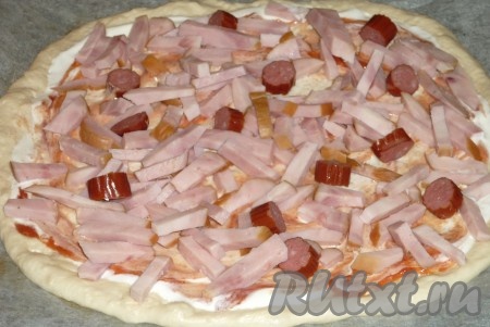 Начинки для такой пиццы могут быть самыми разнообразными. В этот раз я сделала начинку из колбасы и сыра. Тесто сверху смазать 1-1,5 столовыми ложками сметаны (или майонеза) и 1-1,5 столовыми ложками кетчупа. Колбасу нарезать на брусочки или кружочки. Выложить половину нарезанной колбасы поверх теста, смазанного сметаной (или майонезом) и кетчупом.