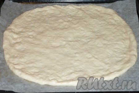 Подошедшее тесто обмять, разделить на 2 части (я предпочитаю из указанного количества ингредиентов формировать 2 пиццы с тонкой основой). Раскатать вначале одну часть теста на столе, присыпанном мукой, в меру тонкий круг, сформировав небольшой бортик, затем переложить на противень, застеленный пергаментом.&nbsp;