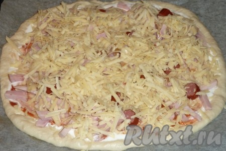 Сыр натереть на крупной тёрке. Посыпать пиццу с колбасой половиной натёртого сыра.&nbsp;