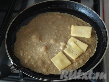 Когда блин подрумянится, перевернуть его на другую сторону. На одну половину блина выложить пластинки твёрдого сыра.

