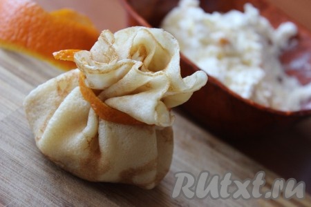 Апельсиновые или мандариновые корочки нарезать на тонкие полоски при помощи ножниц. На середину каждого блина положить одну столовую ложку начинки, края блинчика поднять вверх, формируя мешочек, и обвязать полоской из апельсиновой или мандариновой корочки.
