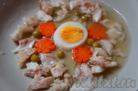 Выложить на тарелку нарезанное вареное яйцо, несколько кусочков рыбы, морковь, зелёный горошек (как на фото). Залить небольшим количеством бульона и отправить в холодильник на 15-20 минут. Таким образом, овощи и рыба не будут плавать в бульоне, что придаст заливному более нарядный вид в конечном итоге.