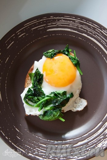 Раздавите зубчик чеснока и разрежьте на 2-4 части. Бросьте его в сковороду, сбрызнутую оливковым маслом, и добавьте листья зелени. Слегка обжарьте зелень и уложите на тост с яичницей. Чеснок потребовался лишь для аромата, его оставьте в сковороде. Тост с яйцом и зеленью готов, приятного аппетита!