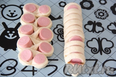 Далее с помощью ножниц нарезать сосиску с тестом на 10-11 частей. Прорезаем только верхнюю часть теста и сосиску. Внизу тесто должно остаться целым и однородным. Затем аккуратно развернуть кусочки сосиски в тесте в разные стороны. Это можно делать на силиконовом коврике или сразу на противне. Также красиво завернуть в тесто все сосиски. 
